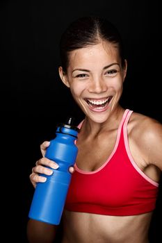 Fitness woman smiling with happy fresh energy while sweating and drinking water from bottle. Chinese Asian / white Caucasian female model on black background.