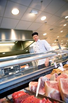 A butcher looking at a fresh meat counter in a grocery store
