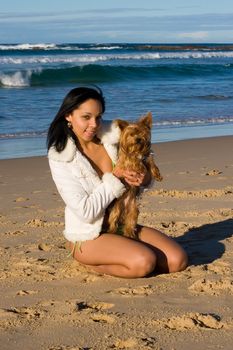 Beautiful model playing with a fluffy brown dog on the beach