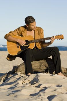 Young man playing his guitar on the beach
