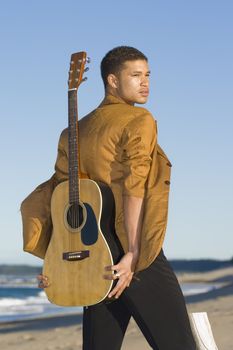 Young man walking with his guitar at the beach