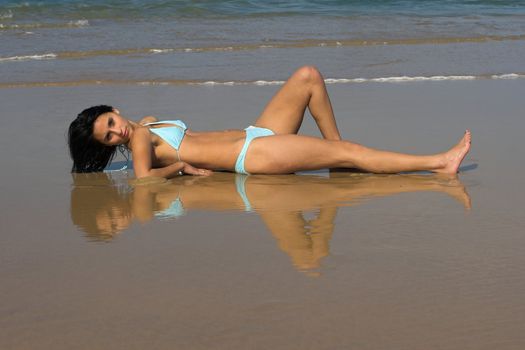 Girl in blue bikini on the wet sand with reflection