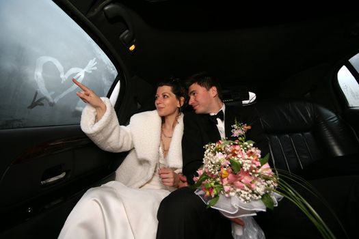 The bride draws heart on glass of the automobile