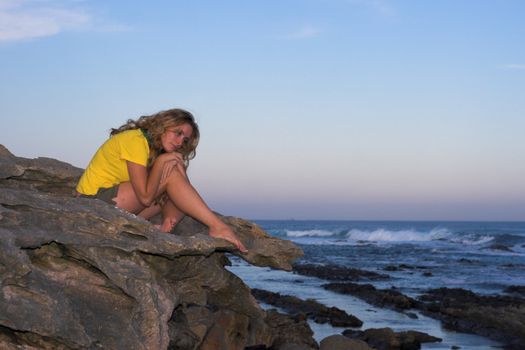 Lonely attractive girl sitting on a rock at the beach