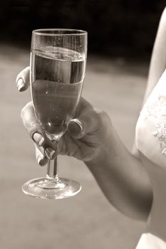 Glass with champagne in hands of the bride. b/w+sepia