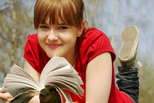 A young girl lying with a book in a spring park          