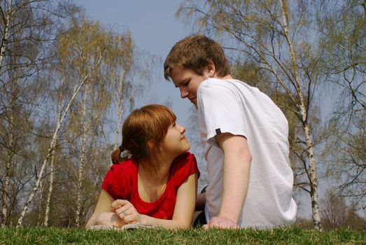 Young girl and a boy - young teenage couple - relaxing on grass in a spring  park   