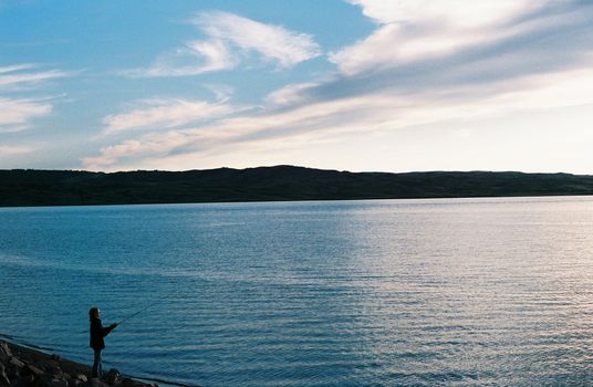 A young girl fishes by the Missouri River in South Dakota, USA as the sun sets.