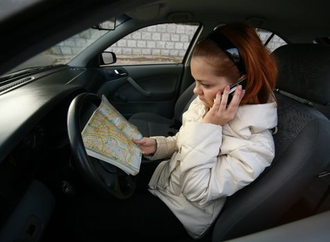 The young girl with a map of streets and the phone in the automobile