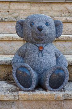 Marble statue of a Teddy Bear sitting on some steps.