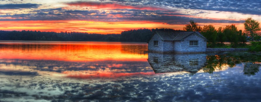 Panorama of a sunrise and pump house utility on a lake.