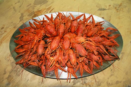 Red boiled crawfishes on the table in oval dish
