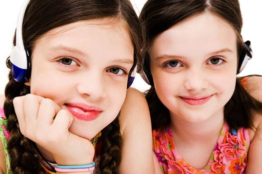 Portrait of two smiling girls listening music on headphones isolated over white