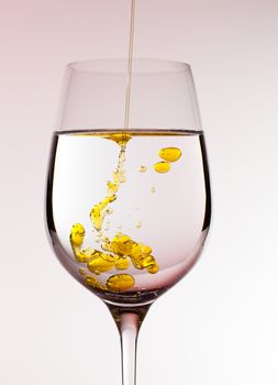 Olive oil being poured into a large wine goblet forming golden bubbles in the liquid