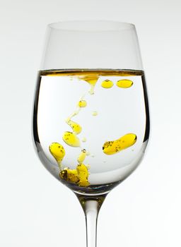 Olive oil being poured into a large wine goblet forming golden bubbles in the liquid