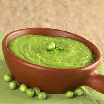 Fresh green pea soup in rustic bowl on jute with copy space (Selective Focus, Focus on the pea and the parsley leaf in the middle of the soup)