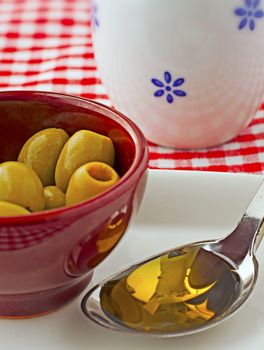 Closeup with shallow depth of field of olive oil in a spoon and olives in a cup