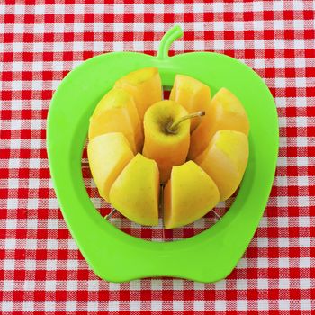 Yellow apple cut by a green tool over white and red cloth