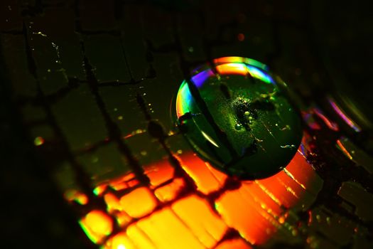 a waterdrop on a cracked CD with bright orange and green colors