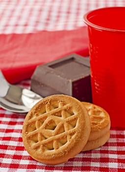 Three biscuits with chocolate, red plastic cup and spoon on the background