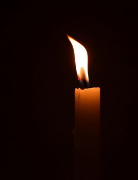 a single burning candle in a dark room