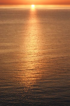 A view from the beach with a yellow glowing sun setting in the horizon. The picture has a warm glow and the sun is reflecting from the water.