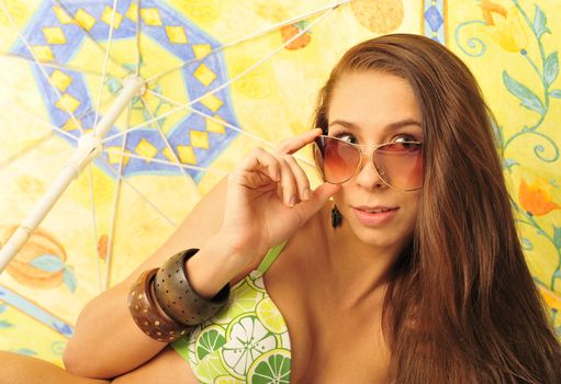 A young and sexy lady in swimsuit and sunglasses under umbrella on a hot day