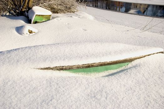 Snow covered boats fragments protruding from snow near river.