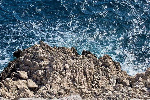 wild blue sea hitting rocky coast and foaming