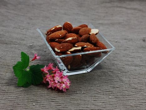 almond in a glass square bowl on tha napkin with flower