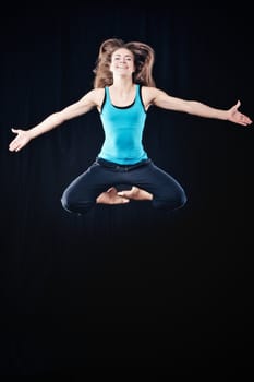Young woman in tracksuit jumping on black background