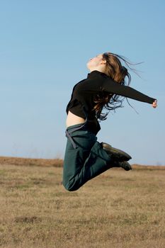 Happy girl jumping around on a dry field