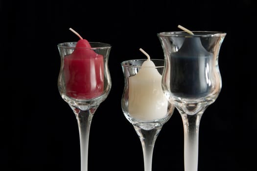 Three unburnt candles in glass candle holders.
