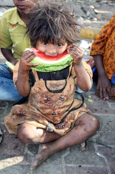 A poor girl from India hungrily eating a watermelon.