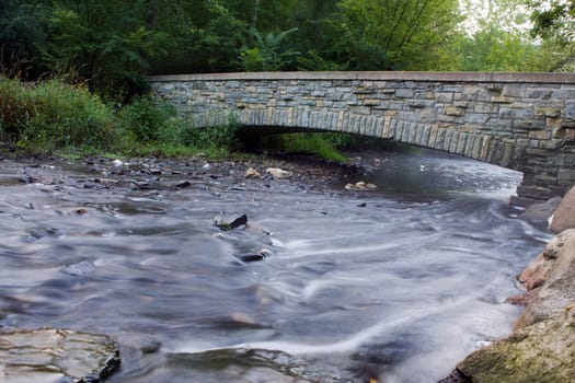 Rushing water of a creek goes under the arch bridge.