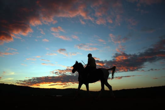 A silhouette of a horserider after sunset, under beautiful skies in twilight colors.