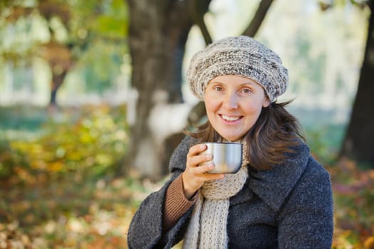 Young pretty woman drinks tea in autumn park