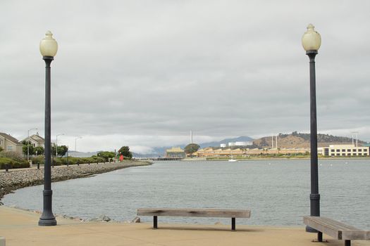 Two street lamps and a bench on pier on cloudy day