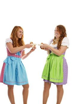two bavarian dressed girls pulling on veal sausages on white background