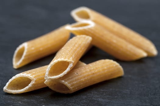 Closeup of dried penne on stone surface.