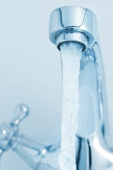 Water tap with a water stream. Blue tone image