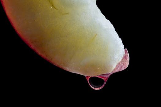 Water drop on a slice of an apple with a black background.