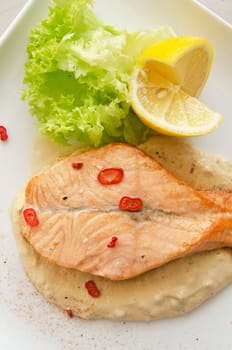 Grilled salmon steak with greens, lemon, sauce and pepper chile