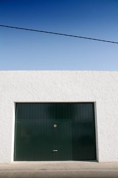 green door garage, white wall and blue sky, sidewalk and street