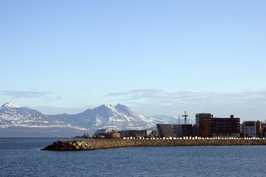 The city of Tromso, Norway. Modern buildings and wave breaker in summer against huge mountains filled with snow. A special and unique sight. 