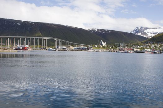 The city of Tromso, Norway. Also known as the capital of the north, Tromso is a famous tourist destination, being the largest city in Northern Norway, as well as a stop-over for the Hurtigruten boats. You can see the famous bridge, Ishavskatedralen - Tromsdalen Church and the landmark of Tromso - Tromsdalstind. Also, notice the snow in summer! 