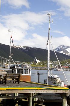A view of the pier and old fishing boats in Tromso. You can see the famous Ishavskatedralen (Tromsdalen Church) and the landmark Tromsdalstind in the background. 