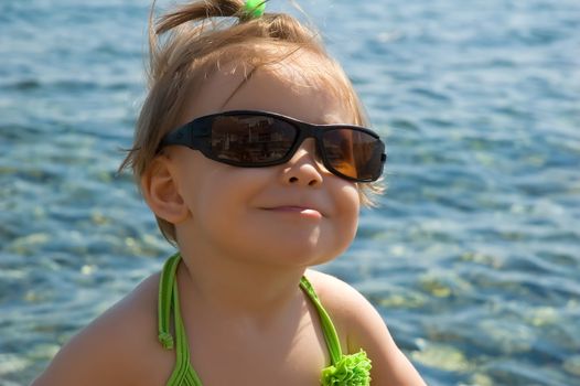 A very cute little girl wearing her mom's sun glasses at the beach