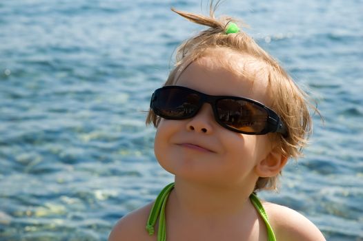 A very cute little girl wearing her mom's sun glasses at the beach