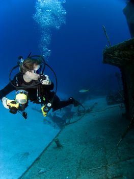 Underwater Photographer looking at a Sunken Ship with Regulator in her hand.